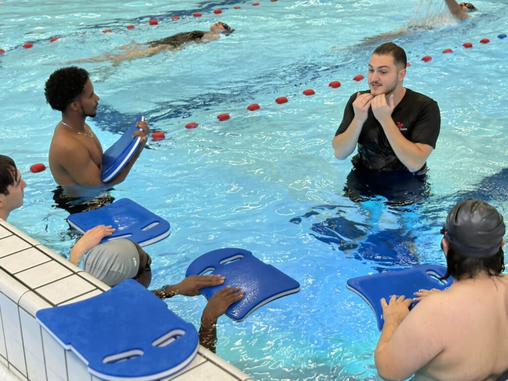 Instructor explaining the next drill to four adults in a shallow lane for beginners